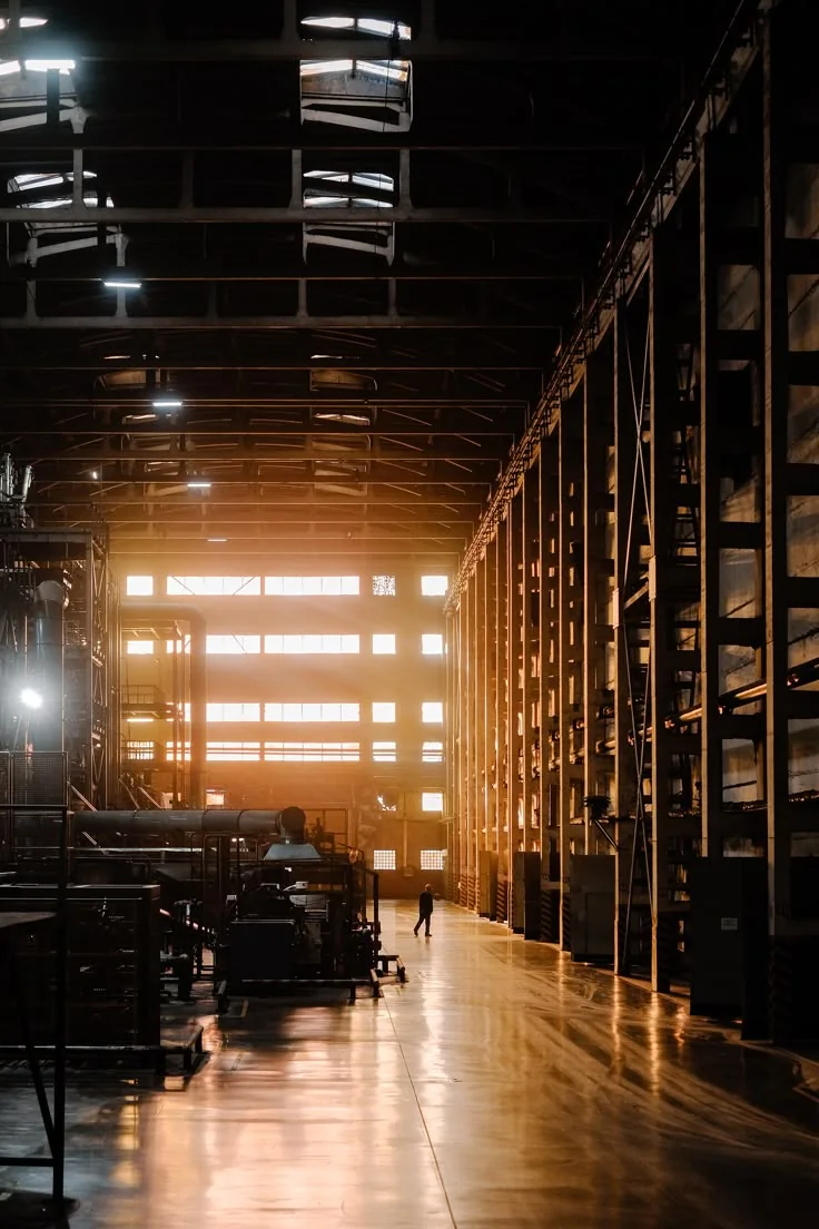 Interior de una planta industrial con maquinaria y luz al fondo